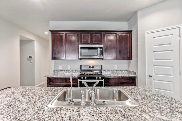 kitchen featuring dark brown cabinetry, appliances with stainless steel finishes, light stone countertops, and sink