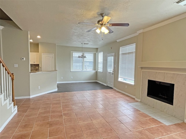 unfurnished living room featuring crown molding, a tile fireplace, a textured ceiling, light tile patterned flooring, and ceiling fan with notable chandelier