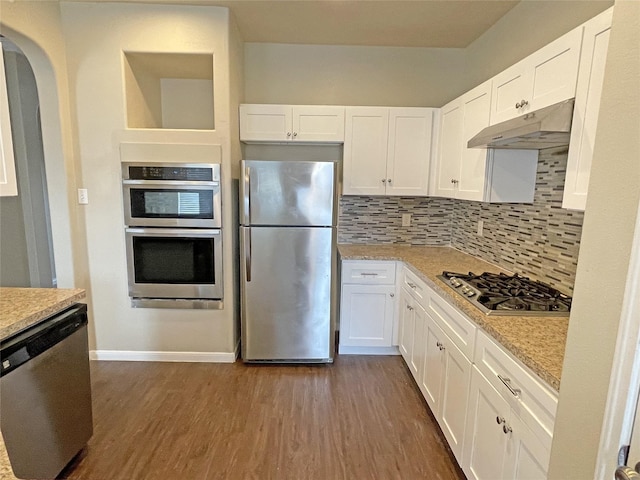 kitchen with appliances with stainless steel finishes, white cabinets, dark hardwood / wood-style flooring, decorative backsplash, and light stone countertops