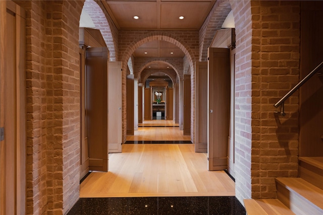 corridor featuring arched walkways, recessed lighting, brick wall, and wood finished floors