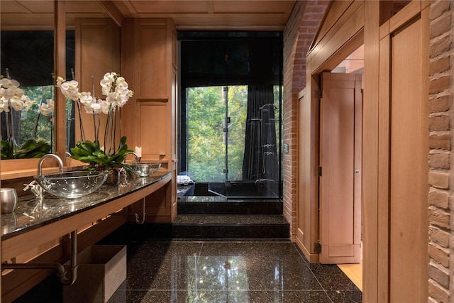 bathroom featuring brick wall, double vanity, granite finish floor, and a sink