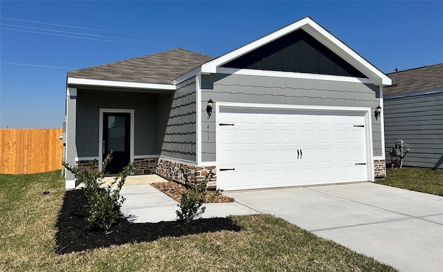 view of front of house with a garage, concrete driveway, stone siding, fence, and a front yard