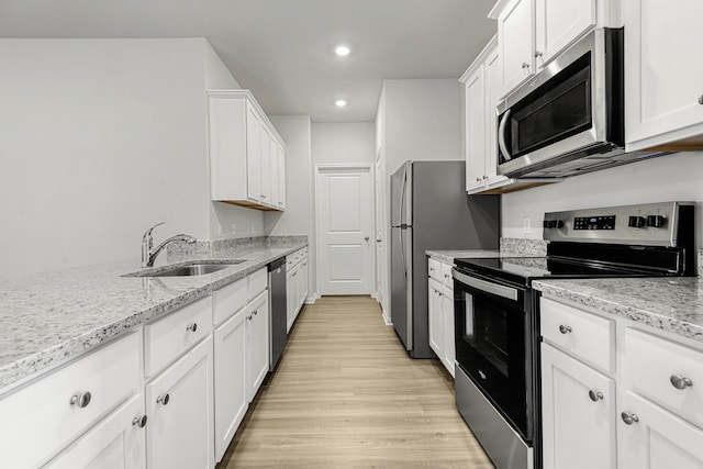 kitchen with appliances with stainless steel finishes, a sink, light stone counters, and white cabinets