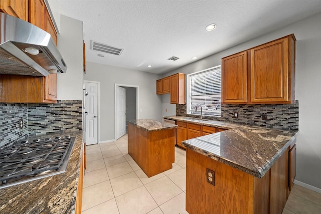 kitchen with sink, dark stone countertops, stainless steel appliances, a kitchen island, and decorative backsplash