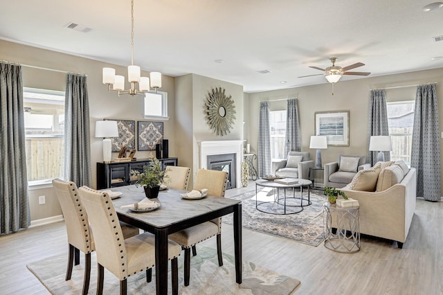 dining space with ceiling fan with notable chandelier, light hardwood / wood-style floors, and a healthy amount of sunlight