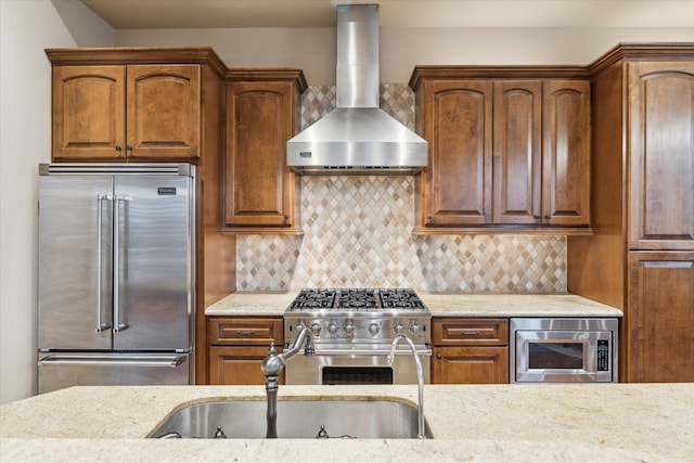 kitchen featuring light stone counters, wall chimney exhaust hood, built in appliances, and backsplash