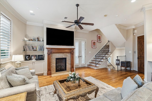 living room with a high end fireplace, light hardwood / wood-style flooring, ornamental molding, and ceiling fan