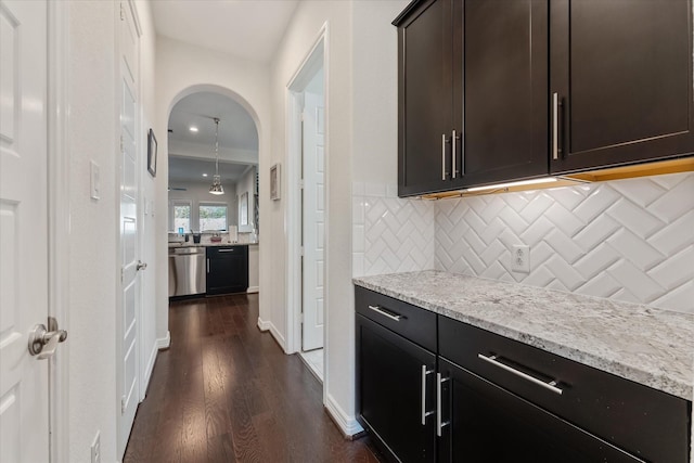 interior space with tasteful backsplash, dishwasher, dark hardwood / wood-style flooring, light stone counters, and dark brown cabinets