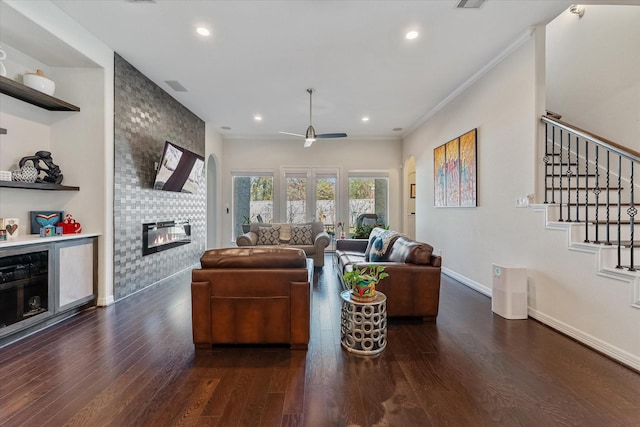 living room featuring crown molding, a large fireplace, dark hardwood / wood-style floors, and ceiling fan