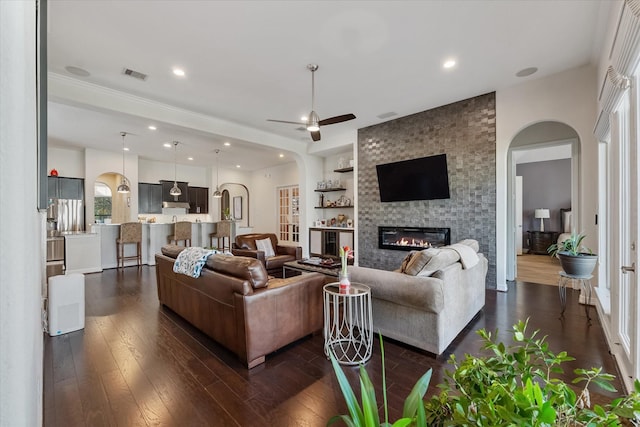 living room with ceiling fan, a large fireplace, built in features, and dark hardwood / wood-style floors