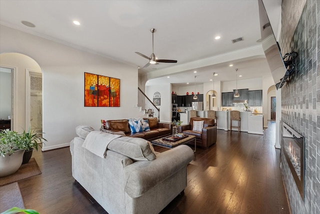 living room featuring a tiled fireplace, dark hardwood / wood-style flooring, ornamental molding, and ceiling fan