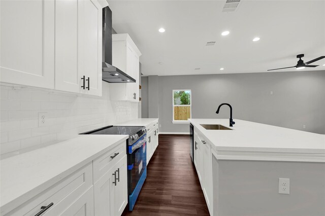 kitchen featuring sink, stainless steel range with electric cooktop, white cabinets, a kitchen island with sink, and wall chimney range hood