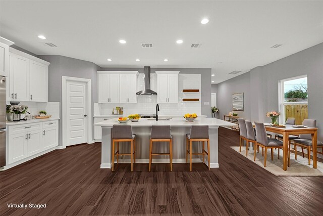 kitchen with a kitchen island with sink, white cabinetry, and wall chimney exhaust hood