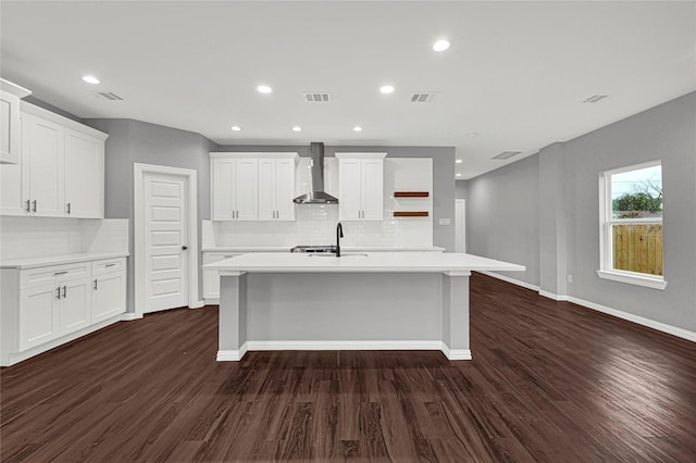 kitchen with white cabinets, wall chimney exhaust hood, a kitchen island with sink, light countertops, and open shelves