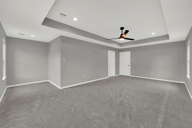 empty room with a tray ceiling, ceiling fan, and carpet flooring