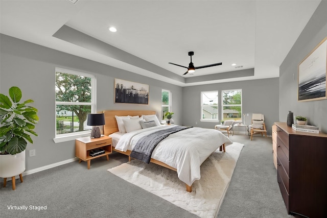 carpeted bedroom featuring ceiling fan and a raised ceiling