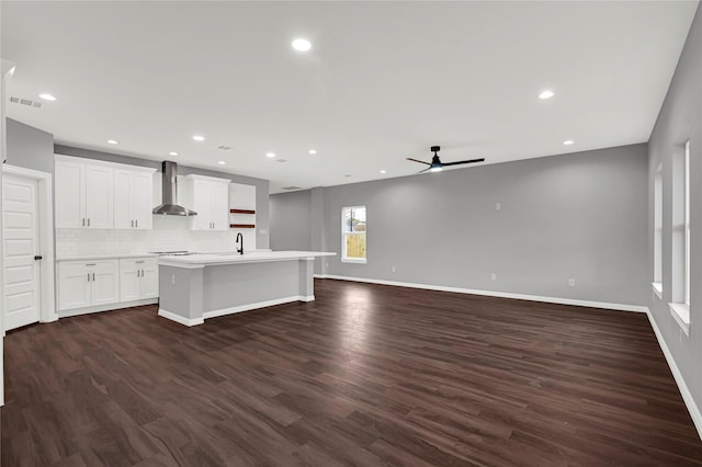 kitchen featuring dark hardwood / wood-style floors, white cabinetry, decorative backsplash, a kitchen island with sink, and wall chimney range hood