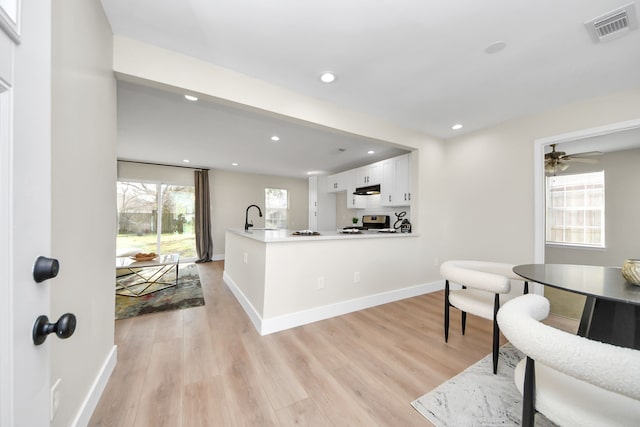 kitchen featuring sink, stainless steel stove, white cabinetry, a healthy amount of sunlight, and kitchen peninsula