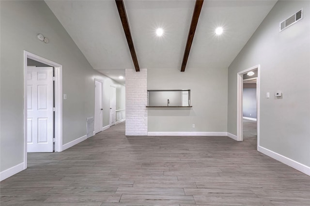 unfurnished living room with vaulted ceiling with beams and light wood-type flooring