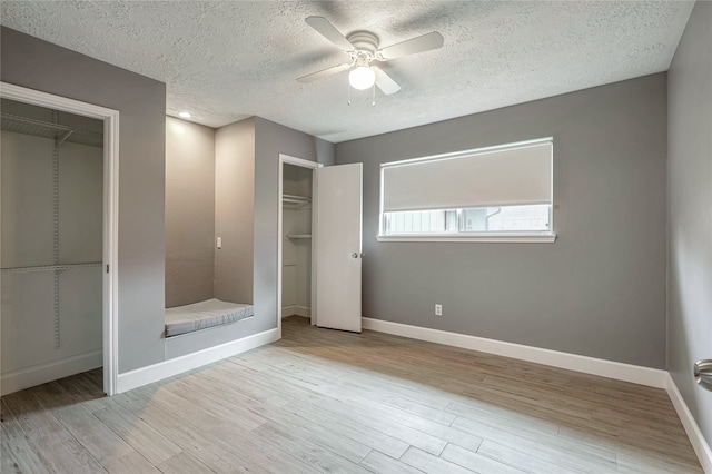 unfurnished bedroom featuring multiple closets, a textured ceiling, light hardwood / wood-style flooring, and ceiling fan