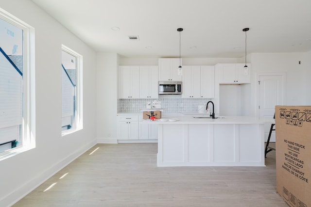 kitchen with a wealth of natural light, white cabinetry, stainless steel microwave, and a sink