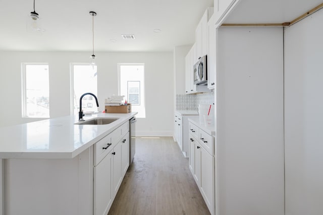 kitchen featuring a kitchen island with sink, stainless steel appliances, a sink, visible vents, and light wood-type flooring