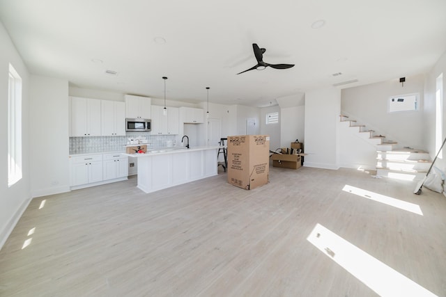 kitchen with light wood finished floors, an island with sink, stainless steel microwave, open floor plan, and backsplash