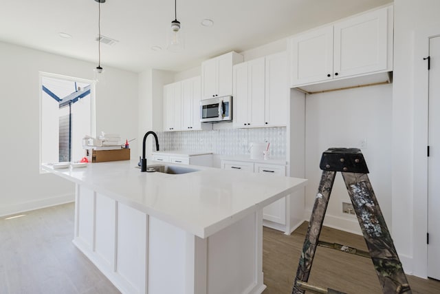 kitchen with visible vents, stainless steel microwave, a sink, light wood-style floors, and backsplash