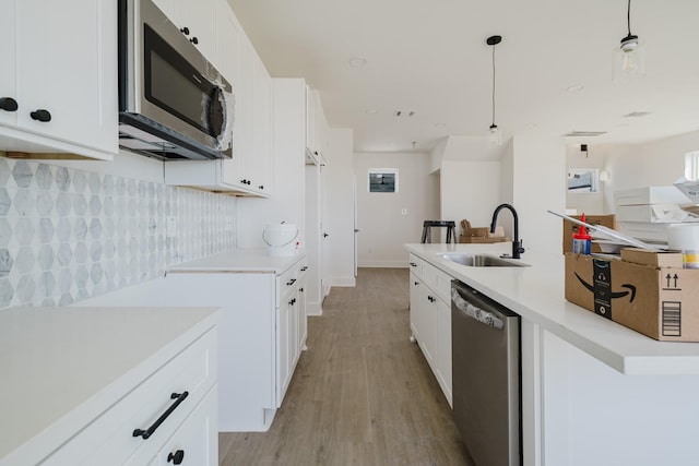 kitchen with tasteful backsplash, appliances with stainless steel finishes, decorative light fixtures, light countertops, and a sink