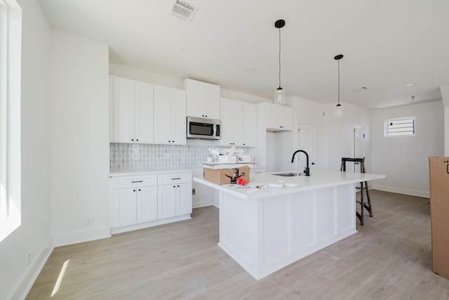 kitchen featuring a center island with sink, light wood finished floors, stainless steel microwave, visible vents, and a sink