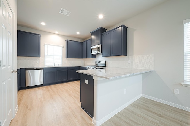 kitchen featuring tasteful backsplash, kitchen peninsula, stainless steel appliances, light stone countertops, and light hardwood / wood-style floors