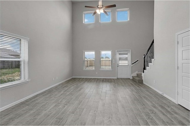 foyer entrance featuring ceiling fan, a towering ceiling, and light hardwood / wood-style floors