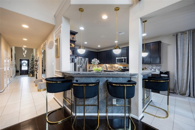 kitchen featuring light tile patterned flooring, appliances with stainless steel finishes, tasteful backsplash, light stone counters, and kitchen peninsula