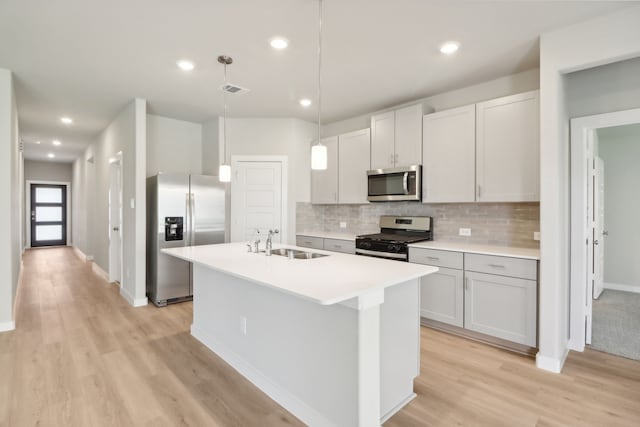 kitchen with pendant lighting, tasteful backsplash, an island with sink, sink, and stainless steel appliances