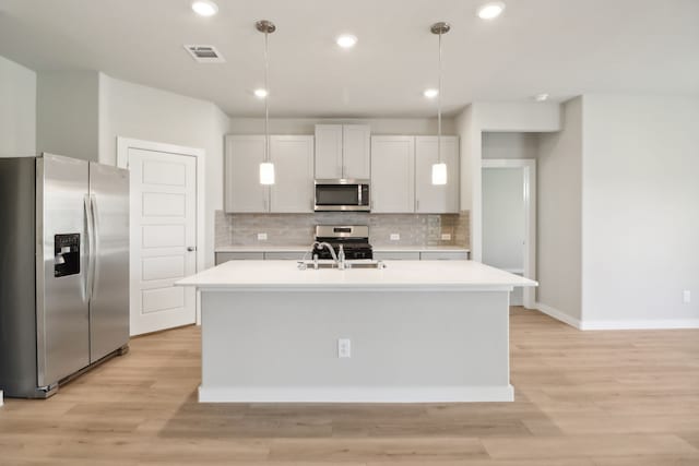 kitchen with white cabinetry, hanging light fixtures, a kitchen island with sink, and appliances with stainless steel finishes