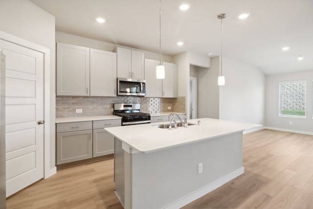 kitchen featuring sink, light wood-type flooring, appliances with stainless steel finishes, pendant lighting, and a kitchen island with sink