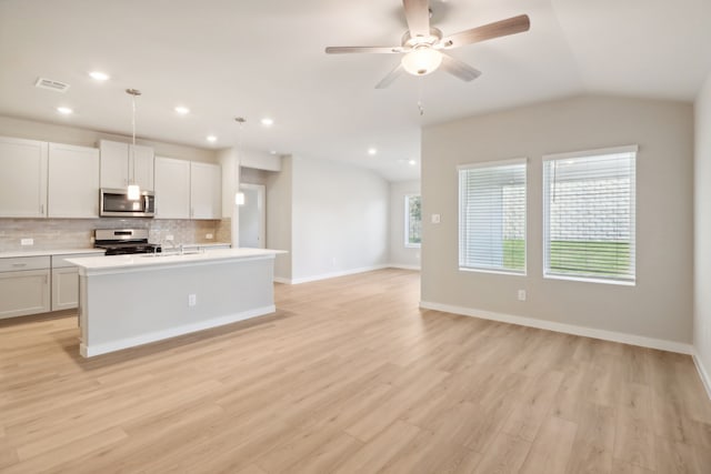 kitchen with vaulted ceiling, appliances with stainless steel finishes, pendant lighting, white cabinetry, and a center island with sink