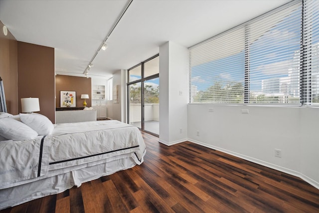 bedroom featuring rail lighting, dark hardwood / wood-style floors, and access to outside