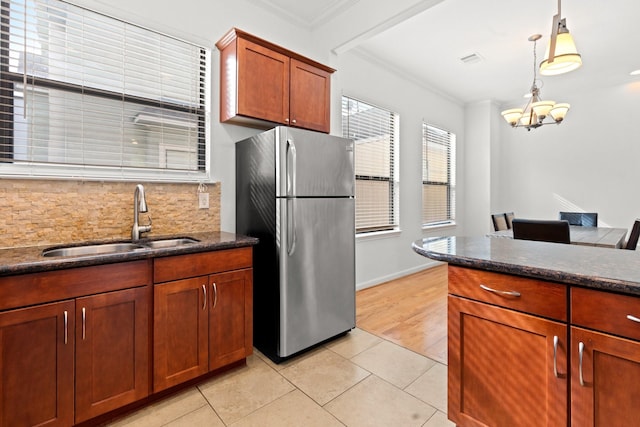 kitchen featuring a sink, dark stone counters, freestanding refrigerator, pendant lighting, and light tile patterned floors