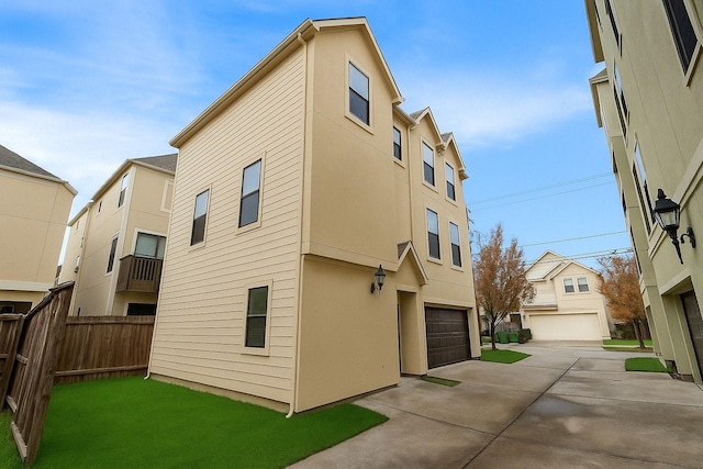 rear view of house with stucco siding, an attached garage, concrete driveway, and fence