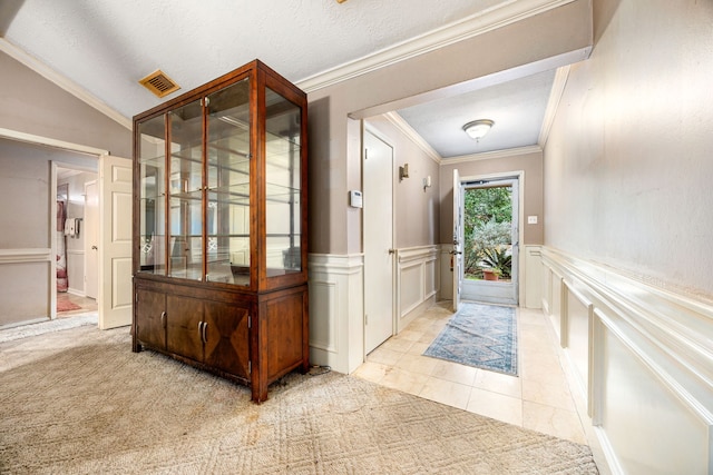 doorway with lofted ceiling, light tile patterned floors, ornamental molding, and a textured ceiling