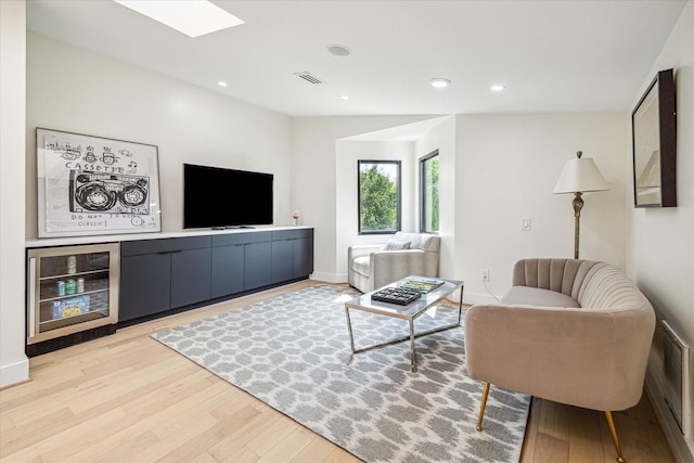 living room with wine cooler, lofted ceiling with skylight, and light hardwood / wood-style floors