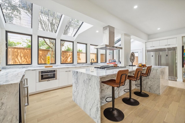 kitchen with white cabinetry, island range hood, appliances with stainless steel finishes, a kitchen island, and light stone countertops