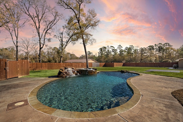 pool at dusk featuring a patio, pool water feature, and a lawn