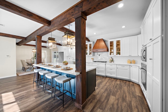 kitchen featuring premium range hood, appliances with stainless steel finishes, white cabinetry, a center island, and beam ceiling