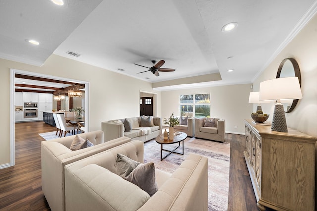 living room with ceiling fan with notable chandelier, dark wood-type flooring, and ornamental molding