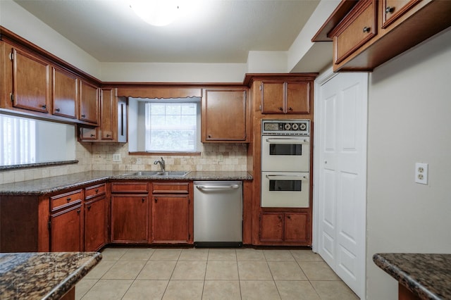 kitchen featuring double oven, dishwasher, sink, dark stone countertops, and backsplash