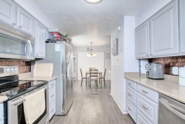 kitchen with pendant lighting, stainless steel appliances, light stone countertops, decorative backsplash, and light wood-type flooring