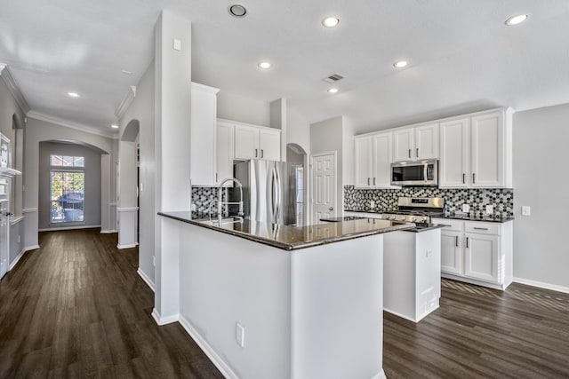 kitchen with appliances with stainless steel finishes, white cabinets, dark hardwood / wood-style flooring, and dark stone counters