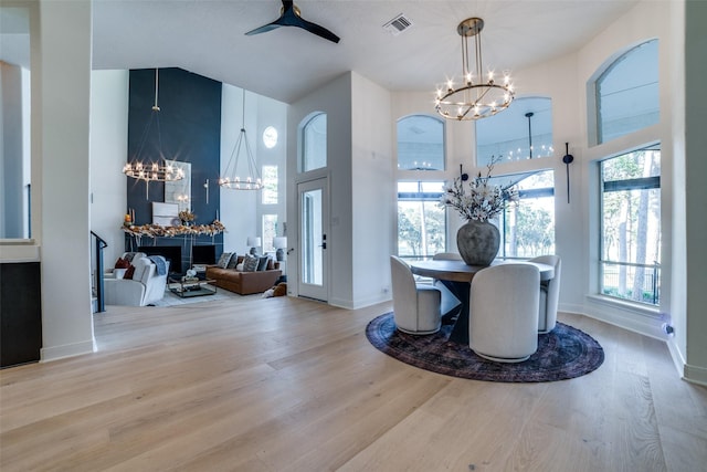 dining room featuring a towering ceiling, light hardwood / wood-style flooring, and ceiling fan with notable chandelier